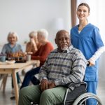 Happy man older patient on wheelchair with female nurse smiling