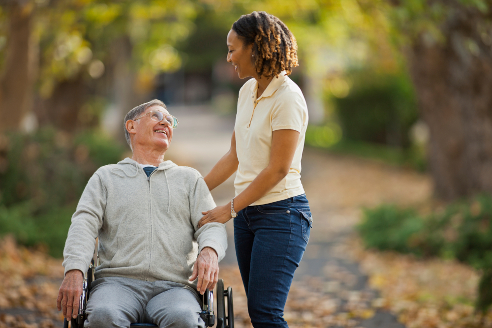 Smiling mid adult nurse assisting an elderly patient in a park.